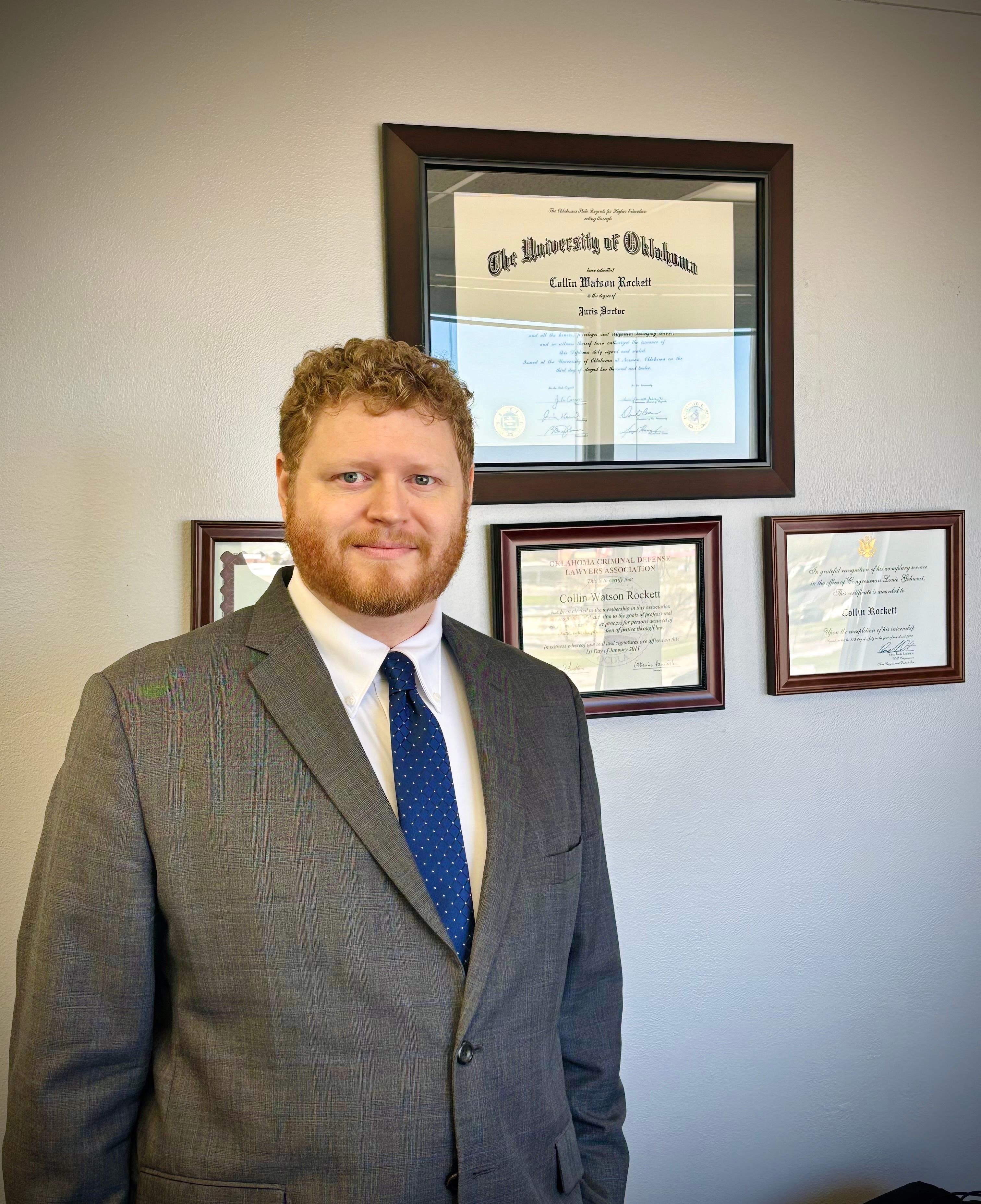 Collin Rockett, Oklahoma criminal defense attorney posing in front of degrees and awards
